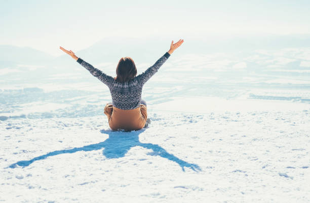 Happy woman sits on the snowy mountain hill over the city. Sunny winter day